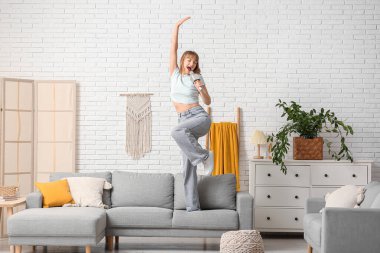 Evdeki gri kanepede mikrofonlu güzel bir kadın şarkı söylüyor.