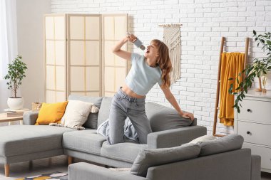 Evdeki gri kanepede mikrofonlu güzel bir kadın şarkı söylüyor.