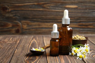 Gerekli yağ şişeleri, ahşap arka planda taze ve kurumuş papatya çiçekleri.