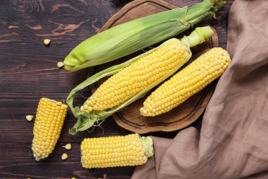 Koyu ahşap masada taze mısır koçanları.