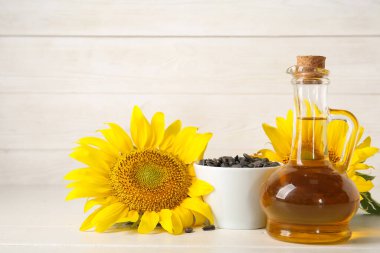 Beyaz ahşap arka planda tohumlu ayçiçeği yağı ve kase süsü.
