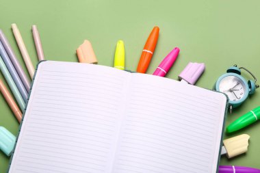 Alarm saati ve yeşil arkaplanda okul kırtasiyesi olan boş bir defter