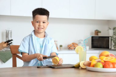 Küçük Asyalı çocuk mutfaktaki masada taze narenciye suyu yapıyor.