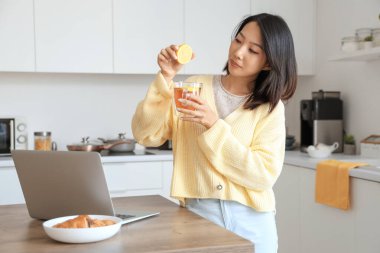 Güzel genç Asyalı kadın mutfakta bir fincan lezzetli çaya limon suyu sıkıyor.