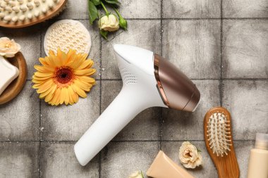 Banyo malzemeleri, kozmetik ürünleri ve grunge gri arka planda güzel çiçeklerle modern fotoepilatör.