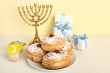 Açık ahşap masada Hanuka kutlaması için donut, hediye, dreidels ve Menorah tabağı.