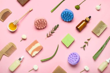 Saç derisi masaj aletleri, şampuan barları, kozmetik ürünleri şişeleri ve pembe arka planda çiçekler.