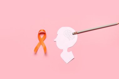 Pembe arka planda turuncu kurdele, kalem ve kağıt insan kafası. Çoklu Skleroz Farkındalık Ayı
