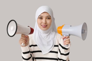 Gri arka planda megafonları olan genç Asyalı Müslüman kadın. Ulusal Duyulma Günü