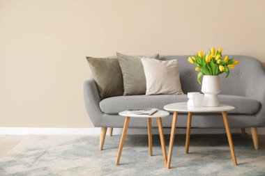 Gri kanepe ve sehpanın üzerinde sarı laleler olan zarif bir iç mekan.