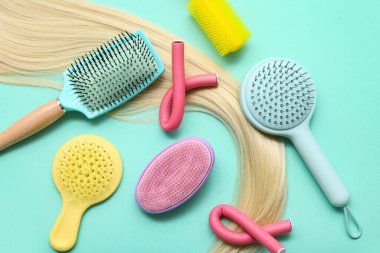 Sarı iplikli farklı saç fırçaları ve turkuaz arka planda bigudiler.