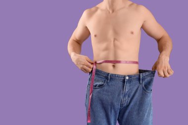 Mor arka planda ölçüm bandı olan bol kotlu yakışıklı genç adam, yakın plan. Kilo verme konsepti