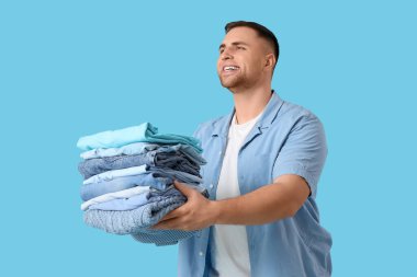 Mavi arka planda bir yığın elbisesi olan genç adam.