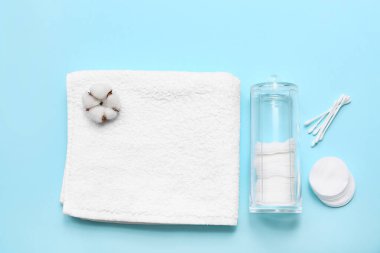 Temiz yumuşak havlu, pamuk pedleri, cam tutacağı, pamuk tomurcukları ve mavi arka planda pamuk çiçeği olan kompozisyon