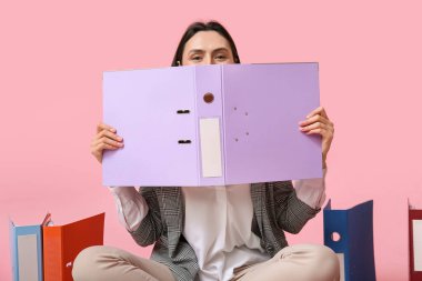 Dosyaları pembe arka planda oturan güzel genç iş kadını.