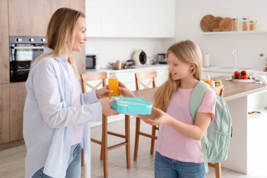 Mutlu anne, mutfakta kızına beslenme çantası ve meyve suyu veriyor.