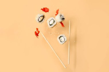 Bej arka planda lezzetli uçan suşi ruloları, zencefil ve çubuklar.