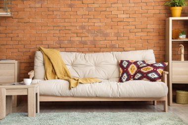 Oturma odasındaki tuğla duvarın yanında ekose ve yastıklı yumuşak kanepe.