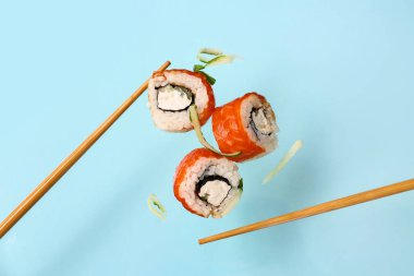 Nefis uçan suşi ruloları, salatalık ve yemek çubukları mavi arka planda.