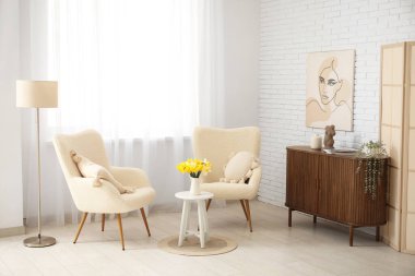 Oturma odasının içinde nergis çiçekleri olan rahat koltuklar ve kahve masası.