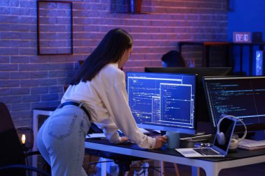 Elinde kahve fincanı olan kadın programcı gece ofiste çalışıyor.