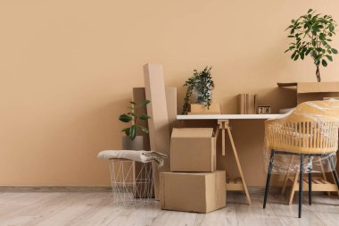 Mobilyalar, ev bitkileri ve bej duvarın yanında eşyalar olan karton kutular. Taşınma konsepti