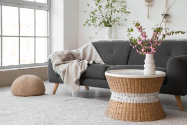 Oturma odasının şık bir iç mekanı. Kanepesi ve çiçek açan dalları olan kahve masası.