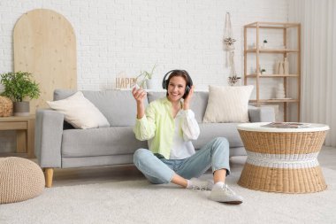 Oturma odasındaki kanepenin yanında klimalı uzaktan kumandalı, gülümseyen genç bir kadın oturuyor.