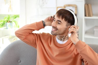 Kulaklıklı genç adam evde müzik dinliyor, yakın plan çekiyor.