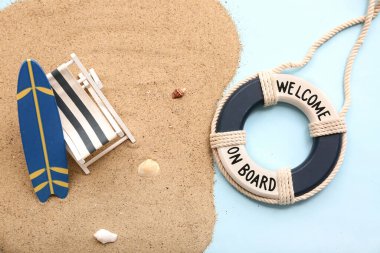 Güverte sandalyesi, sörf tahtası, mavi arka planda kum ve can simidi halkası. Yaz konsepti