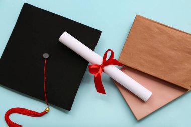 Kırmızı kurdeleli diploma, kitaplar ve açık mavi arka planda mezuniyet şapkası.