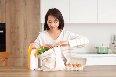 Genç Asyalı kadın mutfaktaki marketten taze ürünleri çıkarıyor.