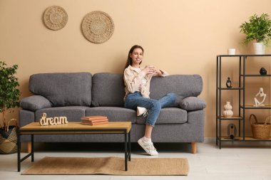 Genç bir kadın elinde fincanla şık bir oturma odasında kanepede oturuyor.