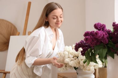 Evinde leylak dalları olan genç bir kadın.