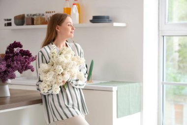 Mutfakta leylak buketleri olan genç bir kadın.