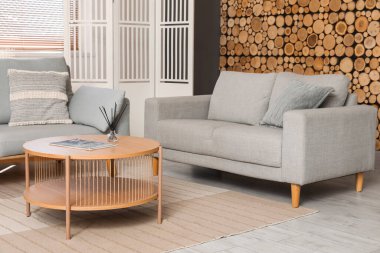 Gri kanepe, sehpa, lamba ve ahşap duvarın yanındaki katlanır ekran oturma odasının içinde.