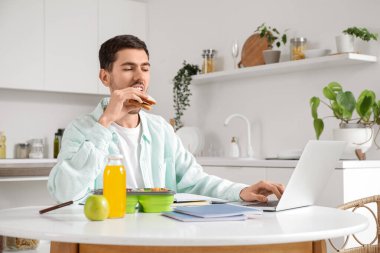 Genç adam mutfakta masa başında çalışırken öğle yemeği yiyor.