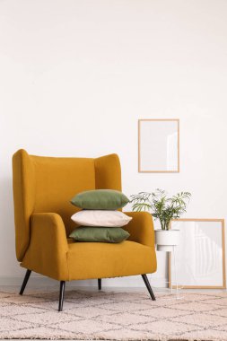 Beyaz duvarın yanında yastık yığını olan rahat bir koltuk.