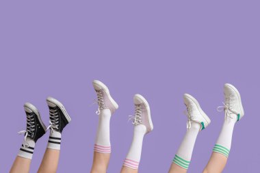 Leylak arka planında farklı spor ayakkabıları olan kadın bacakları.