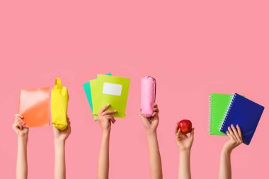 Pembe arka planda defter, elma ve kalem kutusu olan birçok el.