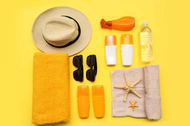 Sarı zemin üzerinde güneş kremi, havlu, şapka ve güneş gözlüğü olan kompozisyon