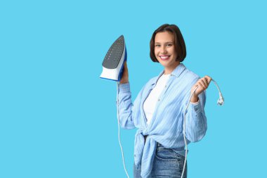 Mavi arka planda demiri olan gülümseyen genç kadın.