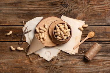 Kabuğu soyulmamış fıstık ve ahşap arka planda bir kaşık fıstık ezmesi olan bir kase.