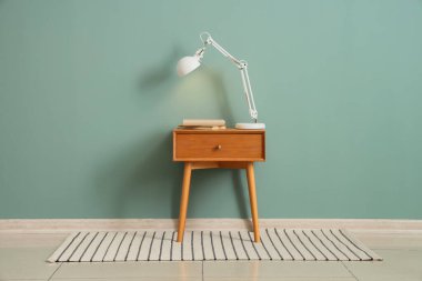 Yeşil duvarın yanındaki masada kitaplarla parlayan lamba.