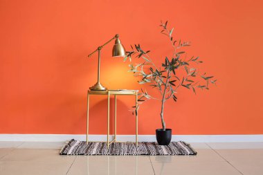 Masada şarjörlü parlayan lamba ve odada turuncu duvarın yanına bitki.