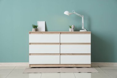 Çiçekli beyaz lamba ve yeşil duvarın yanındaki çekmecelerin çerçevesi.