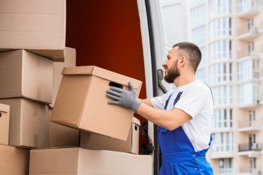 Erkek nakliyeci sokakta arabadan kutuları boşaltıyor.