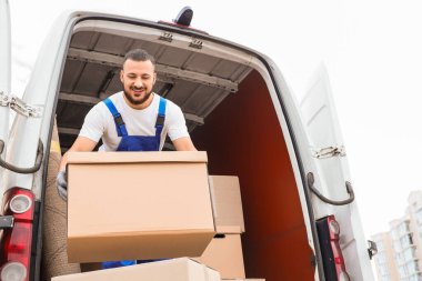 Erkek nakliyeci sokakta arabadan kutuları boşaltıyor.