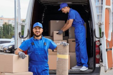 Erkek nakliyeci kutuları boşaltıyor ve sokağa halı seriyor.