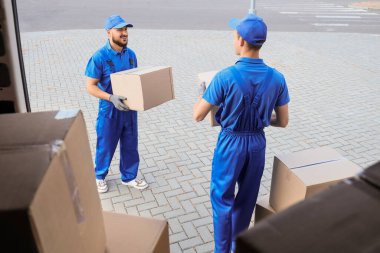 Erkek nakliyeciler sokakta arabadan kutuları boşaltıyor.